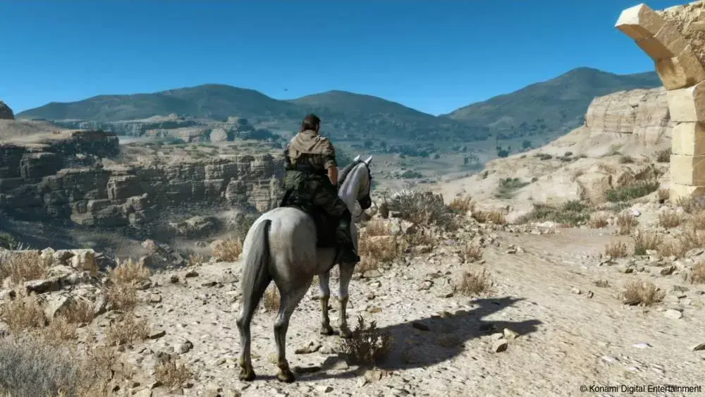 Otwarty świat z gry Metal Gear Solid V. Widok na rozległą pustynię, na pierwszym planie Big Boss na koniu.