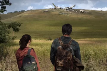 Grafika promocyjna serialu The Last of Us. Tył dwójki postaci, nastoletniej dziewczynki w różowej bluzie z plecakiem na ramieniu oraz mężczyzny w dżinsowej kurtce, którzy wpatrują się we wrak samolotu znajdujący się na pobliskim wzgórzu.