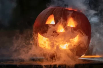 Gry na Halloween. Twarz wycięta w dyni, ze środka dobiega pomarańczowe światło, a dynia spowita jest mgłą