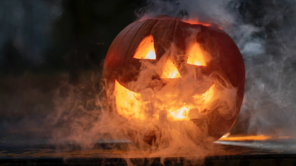 Gry na Halloween. Twarz wycięta w dyni, ze środka dobiega pomarańczowe światło, a dynia spowita jest mgłą