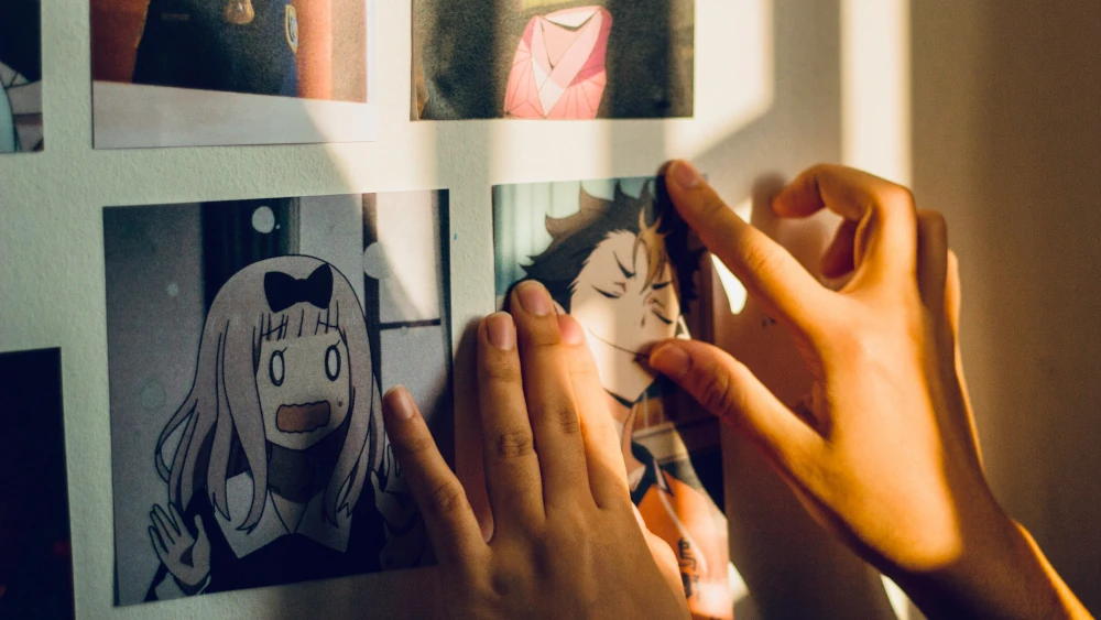 Dłonie przyklejające grafiki z anime na ścianie