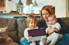 Cyfrowy prezent na Dzień Dziecka — mama z dziećmi siedząca na kanapie i pokazująca ekran tabletu