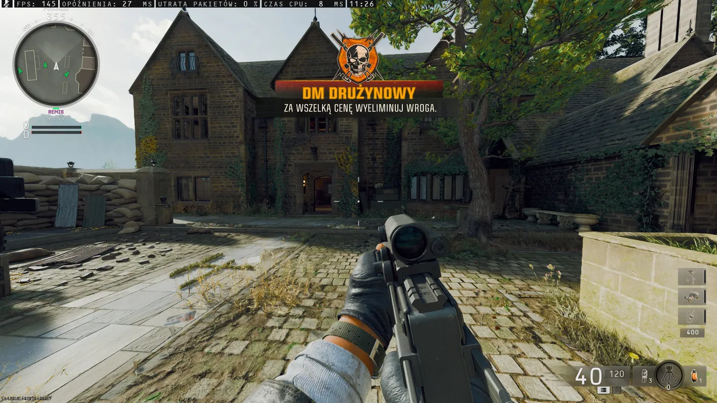 Ten obraz przedstawia silnie ufortyfikowany budynek w wiejskim, zalesionym otoczeniu. Nad wejściem wyświetlany jest duży symbol czaszki i krzyża, wskazujący, że jest to baza wrogiej frakcji. Gracz spogląda przez lunetę broni, prawdopodobnie przygotowując się do walki z wrogami znajdującymi się na terenie kompleksu.