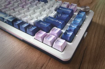 Klawiatura mechaniczna Redragon Cyrus Pro z keycapami w stylu anime, w odcieniach niebieskiego, fioletowego i białego, na tle drewnianego blatu. Widoczny metalowy pokrętło i elegancki design podkreślają unikalny charakter urządzenia.