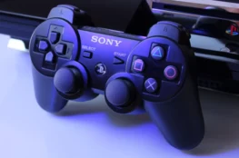 Klasyczny kontroler PlayStation 3 (DualShock 3) w niebieskim oświetleniu na ciemnym tle. To właśnie PS3 z wbudowanym napędem Blu-ray pomogło formatowi wygrać wojnę formatów z HD DVD.