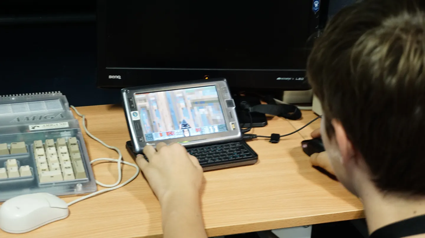 Młody uczestnik testuje grę na nowoczesnym, przenośnym urządzeniu z klawiaturą, obok klasycznego komputera Amiga 1200. Połączenie starej i nowej technologii przy jednym stanowisku