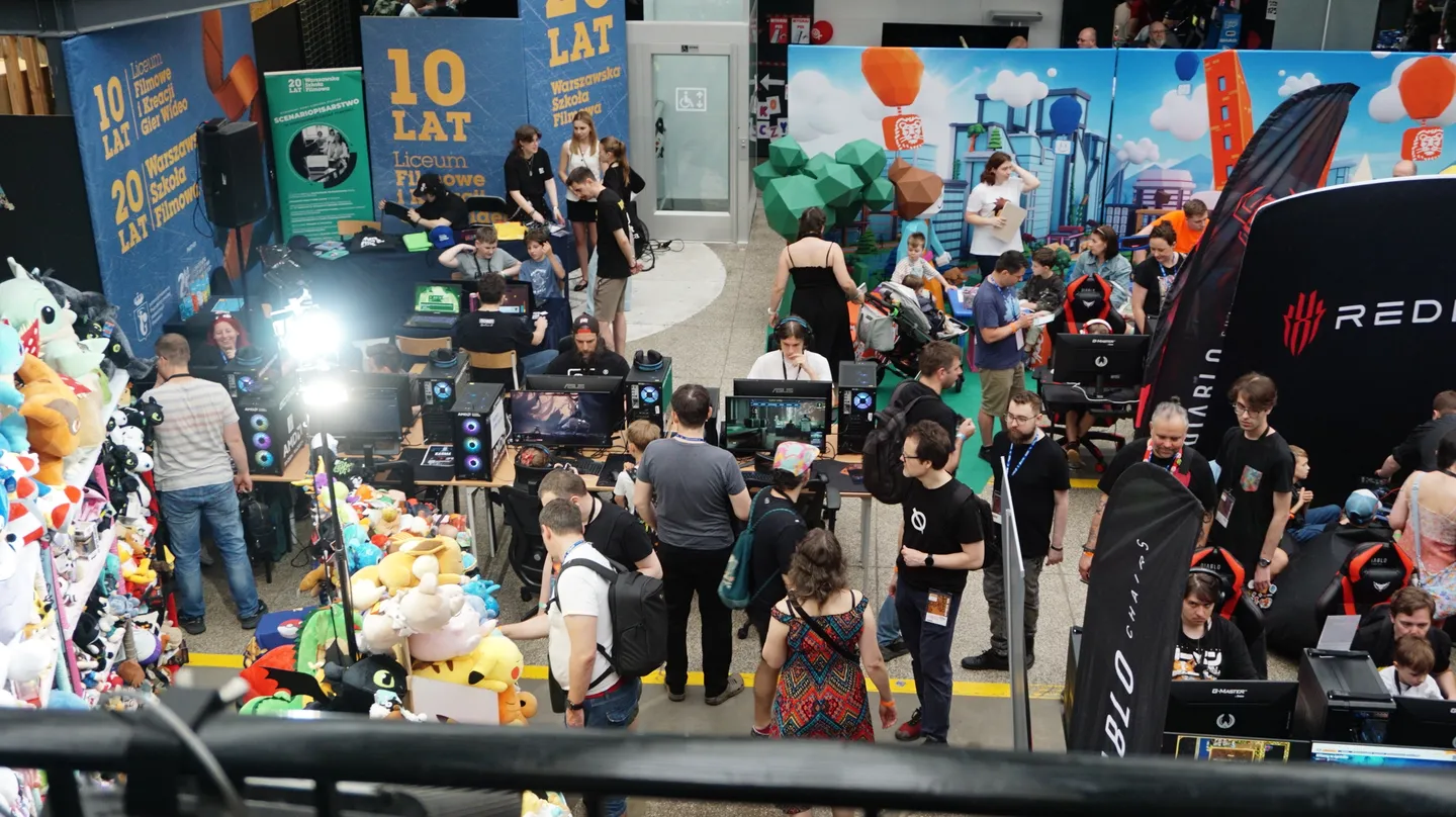 Widok na zatłoczoną halę Pixel Heaven 2025 &ndash; liczne stanowiska z komputerami, stoisko z maskotkami oraz uczestnicy testujący nowe i klasyczne gry