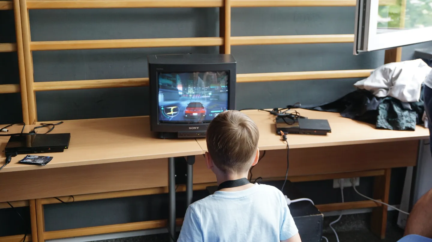 Chłopiec gra w wyścigi samochodowe na klasycznej konsoli PlayStation 2 podłączonej do telewizora CRT w strefie retro Pixel Heaven 2025