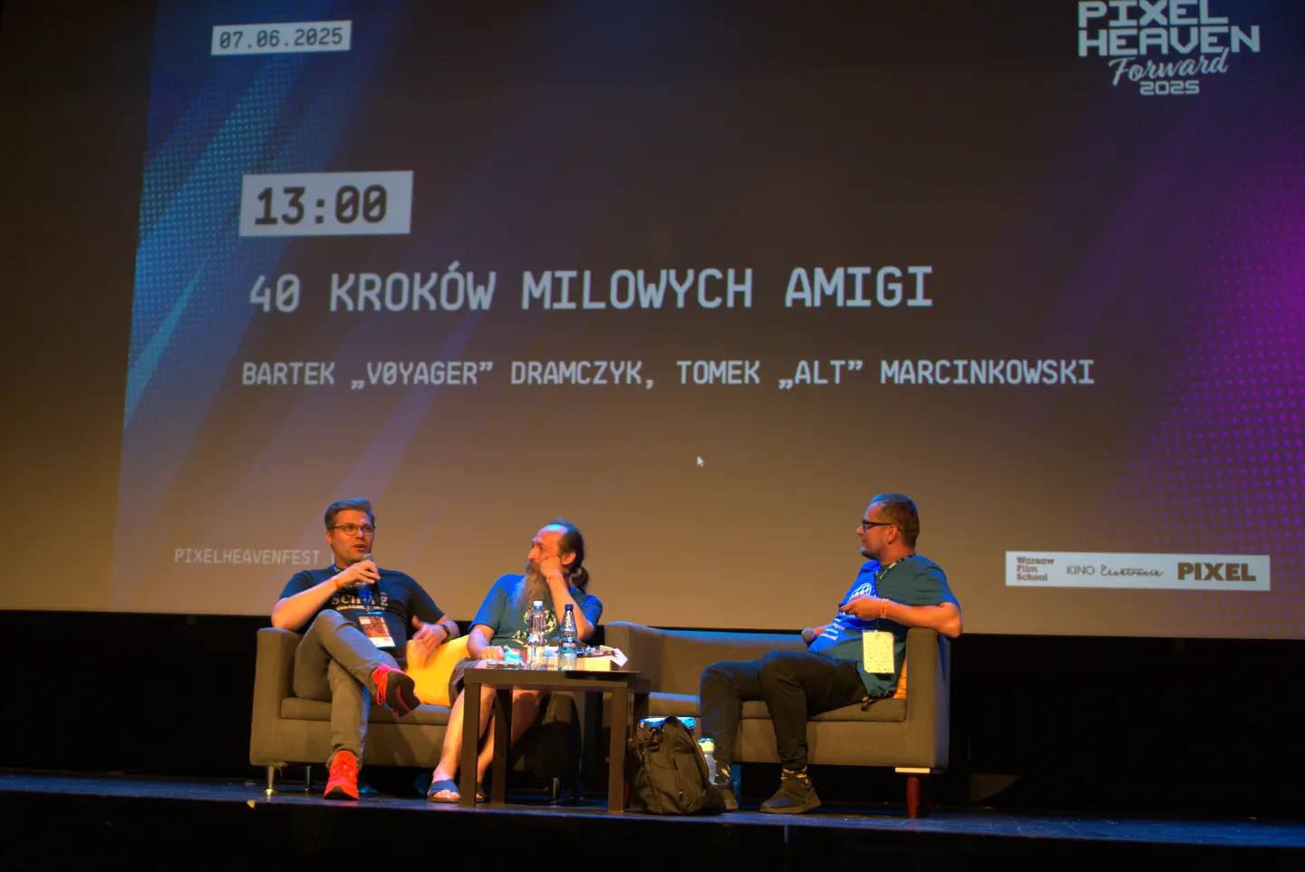 Prelekcja &bdquo;40 krok&oacute;w milowych Amigi&rdquo; na Pixel Heaven 2025. Trzech ekspert&oacute;w siedzi na scenie i omawia najważniejsze momenty w historii kultowego komputera Amiga, z wyraźnie wyeksponowanym tytułem prezentacji w tle