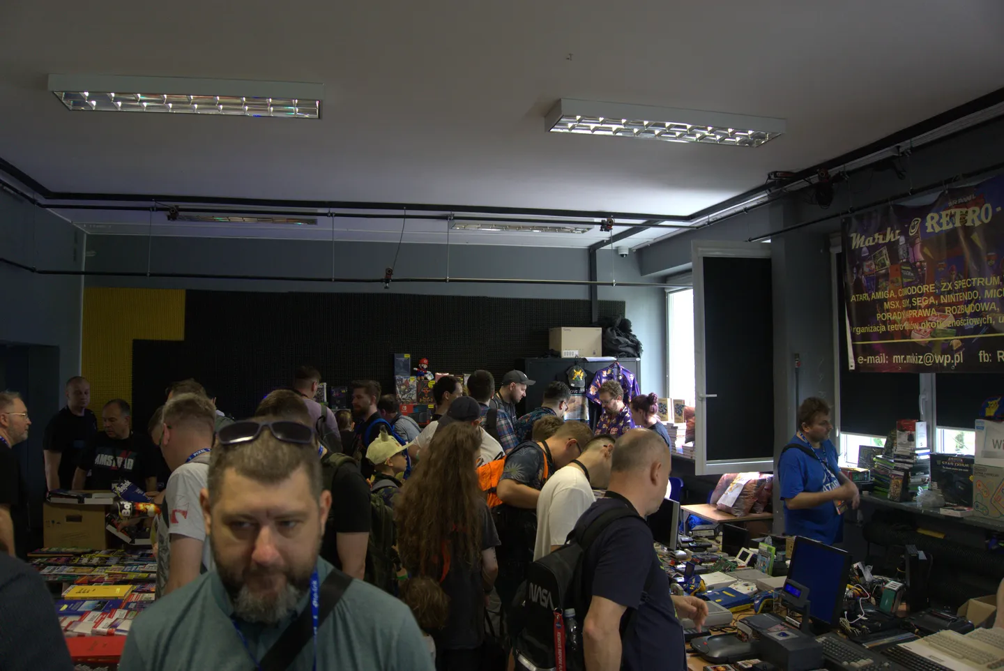 Tłum odwiedzających na stoiskach z retro sprzętem i grami podczas Pixel Heaven 2025. Widać entuzjast&oacute;w przeglądających kolekcje konsol, komputer&oacute;w i gier, a także wymieniających się doświadczeniami.