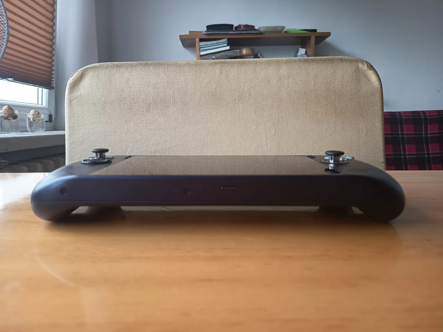 Widok z tyłu na przenośną konsolę do gier leżącą na stole, z widocznymi przyciskami i portem pośrodku obudowy.