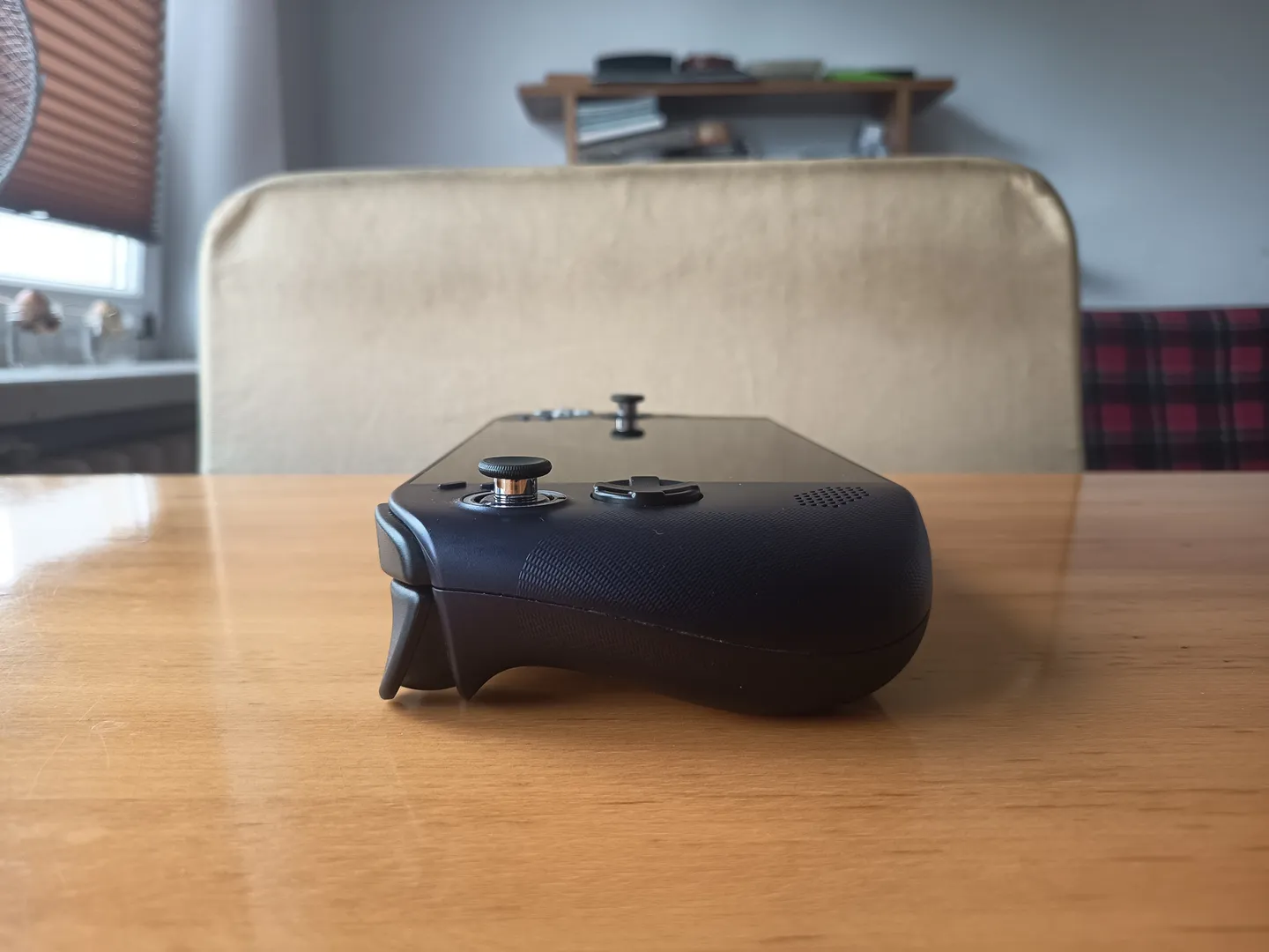 Widok z boku na przenośną konsolę do gier leżącą na stole, z wyraźnie widocznym lewym uchwytem, gałką analogową i przyciskiem.