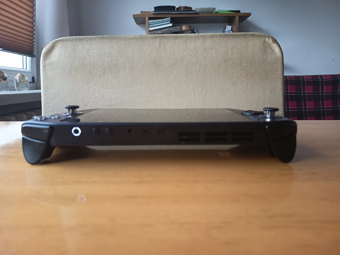 Widok z przodu na przenośną konsolę do gier leżącą na stole, pokazujący porty, przyciski i analogowe gałki po bokach urządzenia.