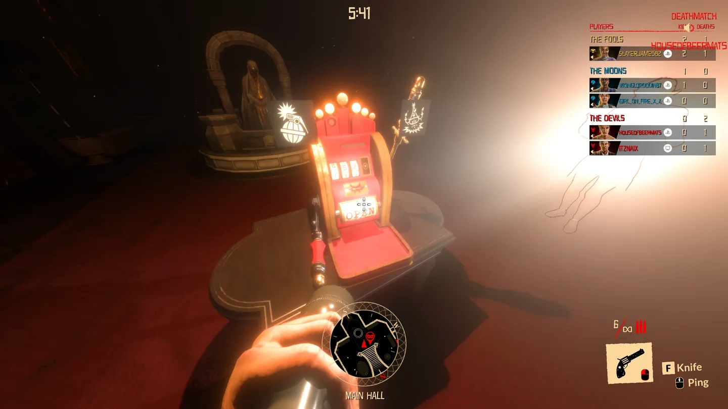 Drugi obraz ukazuje widok z pierwszej osoby na jasne, rozświetlone pomieszczenie z czerwonym dywanem, maszyną do gry i statuetą na piedestale w tle; na pierwszym planie widoczne są dłonie postaci z latarką, a w prawym g&oacute;rnym rogu panel punktacji drużynowej.