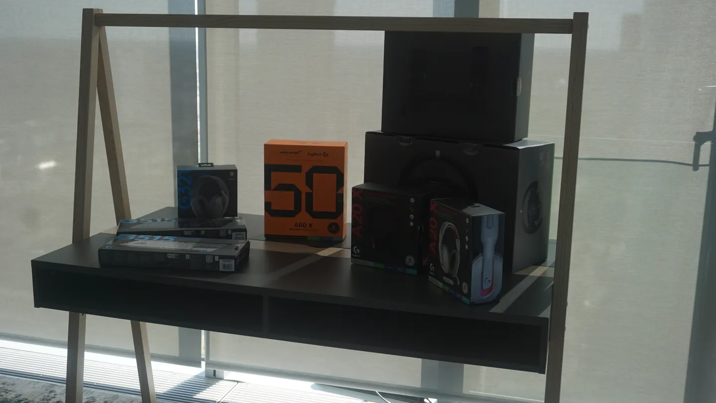 Wyeksponowane opakowania najnowszych akcesoriów gamingowych Logitech — słuchawki, myszki oraz klawiatury — ustawione na designerskim regale, gotowe do testów podczas prezentacji.