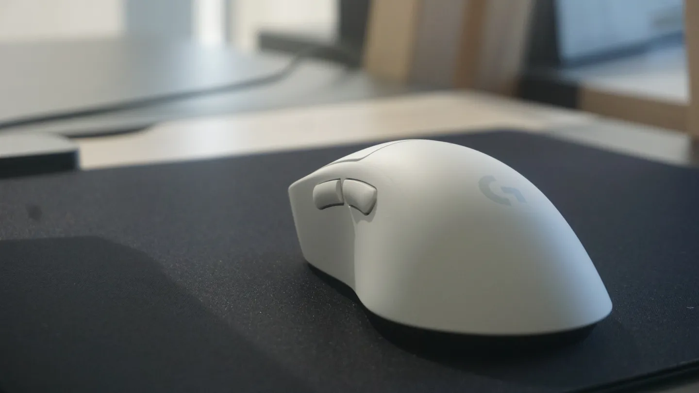 Nowoczesna bezprzewodowa mysz gamingowa Logitech w białej wersji kolorystycznej, prezentowana na ciemnej podkładce biurkowej w stonowanym świetle.