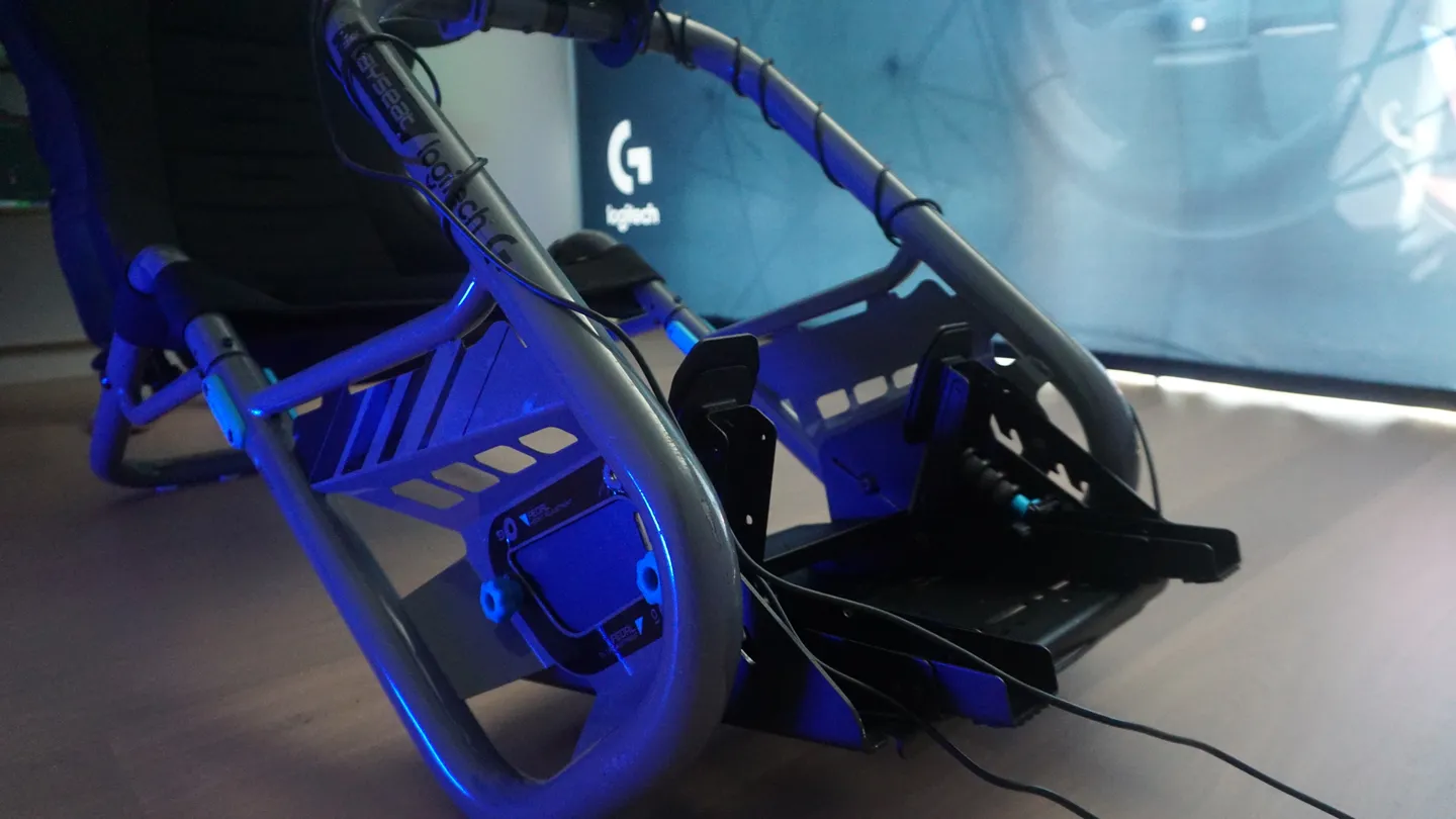 Nowoczesny kokpit do symulatora wyścigów z zamontowanymi pedałami i solidną metalową ramą na tle niebieskiego światła.