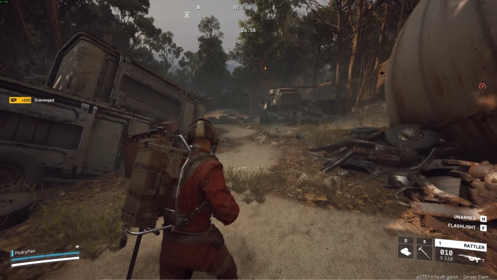 Widok zza pleców postaci gracza ubranego w czerwony kombinezon i plecak ze sprzętem, przemierzającego opuszczony, zalesiony teren z wrakami pojazdów i śmieciami. Po lewej stronie leży przewrócony kontener, a po prawej znajduje się zardzewiała, duża beczka i stos złomu. Na ekranie widoczny jest interfejs z informacją o zdobytym doświadczeniu.