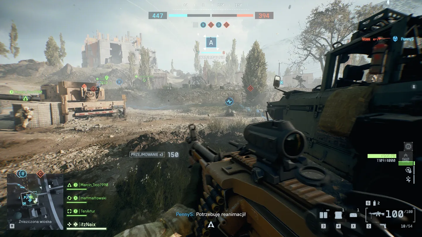 Widok przez celownik karabinu w kierunku punktu E, chronionego przez worki z piaskiem i zabudowania; ekran pokazuje efekt postrzał&oacute;w, HUD z obroną punktu i wskaźnikami liczby obecnych graczy.