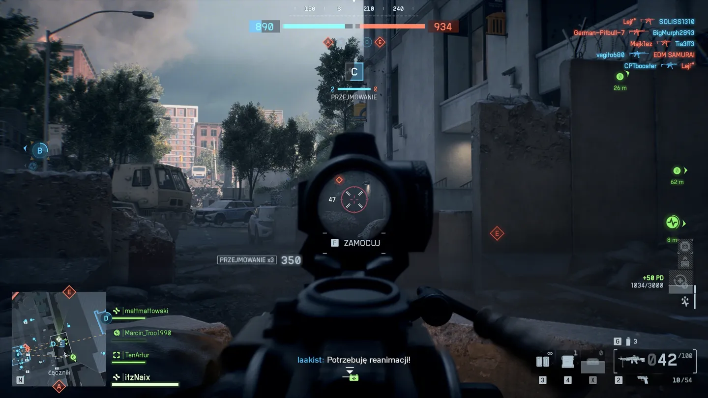 Widok przez celownik optyczny na punkt kontrolny w zniszczonym mieście; w tle widać pojazdy, barykady i zaludnione ulice, a na ekranie interfejs przejmowania punktu oraz komunikaty drużynowe.