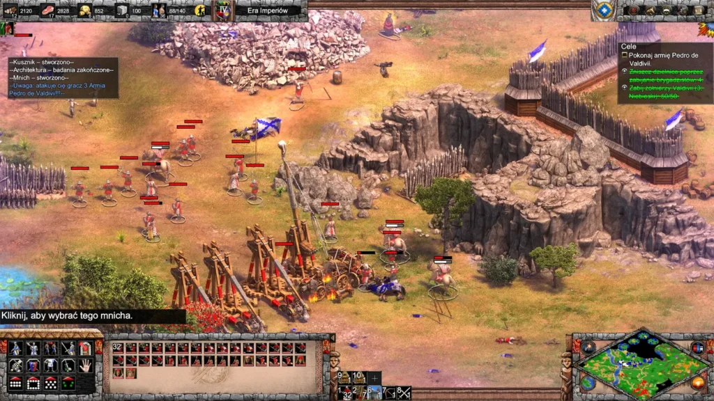 Oblężenie zamku Celtów w Age of Empires II: Definitive Edition – The Last Chieftains: niebieskie mury i wieże atakowane przez czerwone trebusze i piechotę, armia na pustynnym terenie z drzewami i skałami.