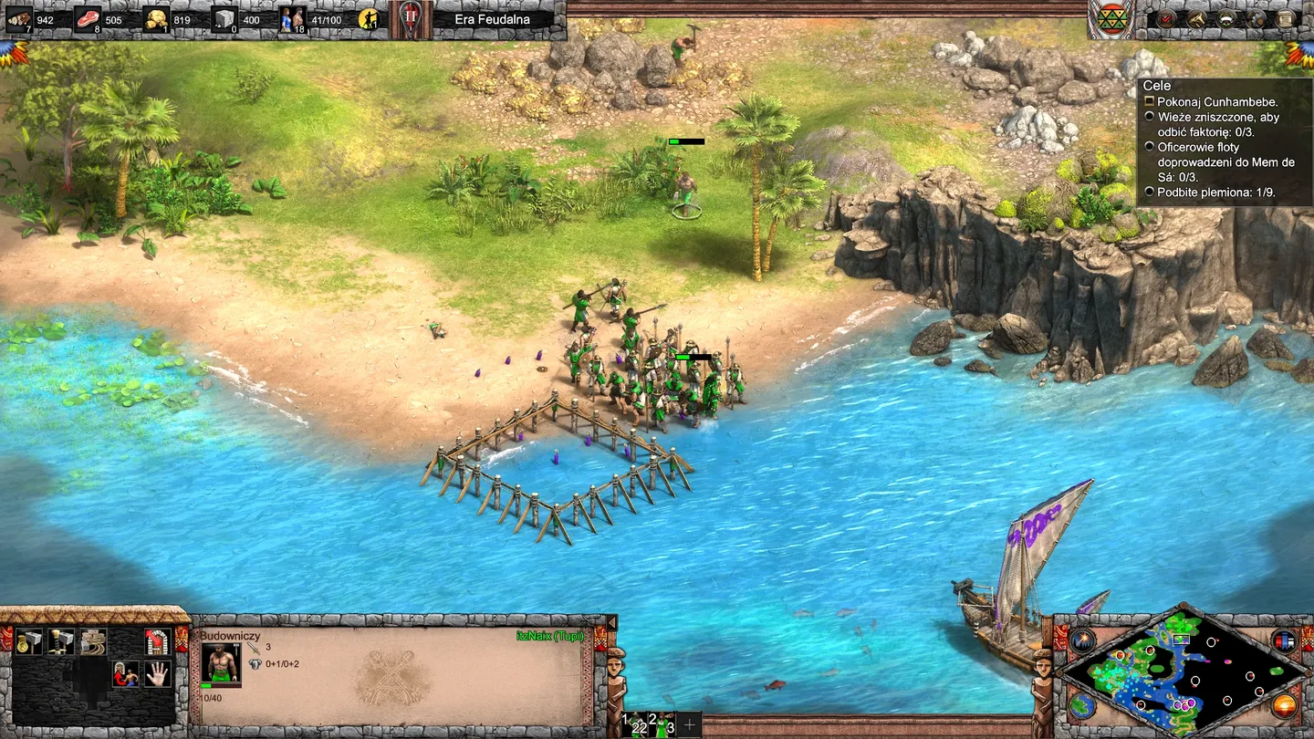 Scena nadbrzeżna z cywilizacją Tupi lub Muisca w Age of Empires II: Definitive Edition &ndash; The Last Chieftains: fioletowe oddziały przy drewnianym pomoście, żagle na wodzie, tropikalne drzewa i klify nad turkusowym morzem. ​