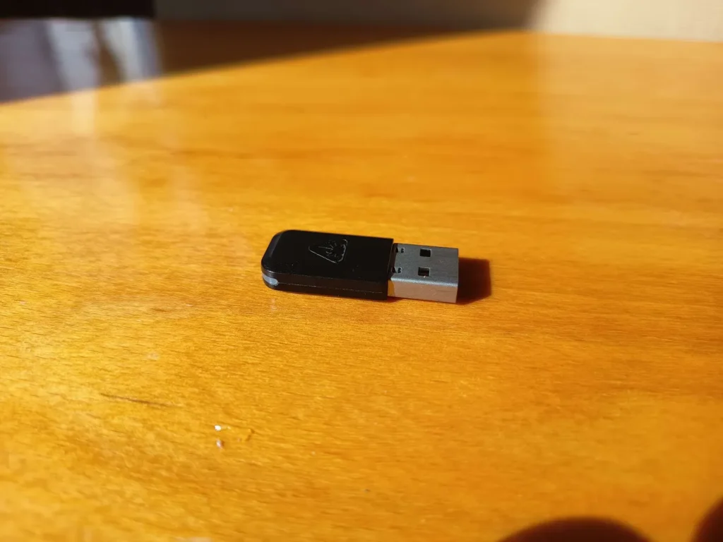 Czarny dongle USB bezprzewodowy Turtle Beach do słuchawek Stealth 600 Gen 3 z logo firmy, leżący na drewnianym stole.
