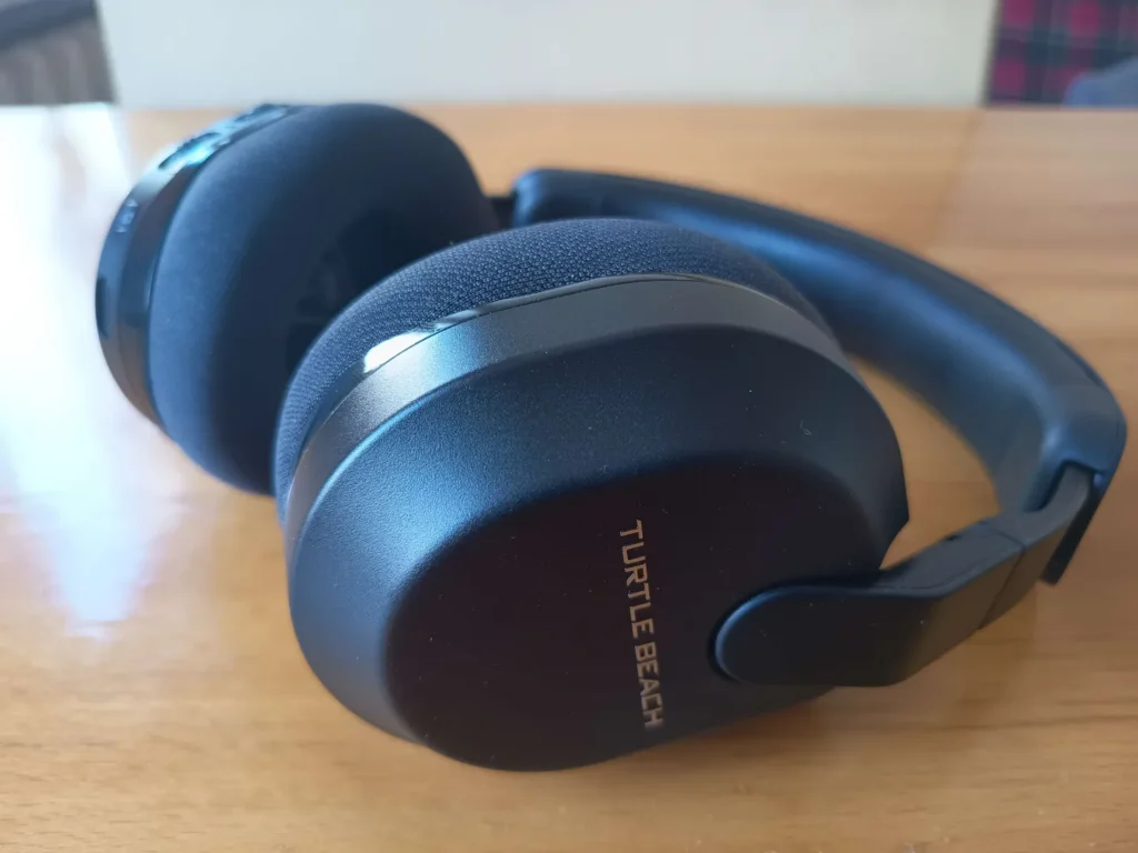  Pełny widok bezprzewodowych słuchawek gamingowych Turtle Beach Stealth 600 Gen 3 w czarnym kolorze z logo na obudowie, stojących na drewnianym stole.