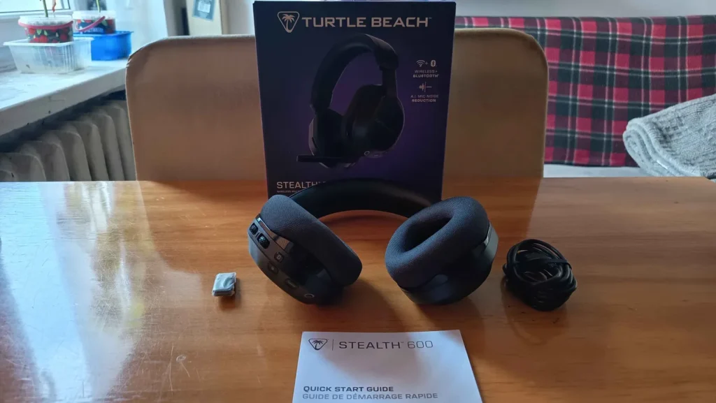Słuchawki Turtle Beach Stealth 600 Gen 3 w kolorze czarnym, ułożone na drewnianym stole obok kabla, szybkiej instrukcji i pudełka produktu.