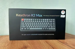 Pudełko Keychron K2 Max QMK na drewnianym blace na tle szarej ściany,