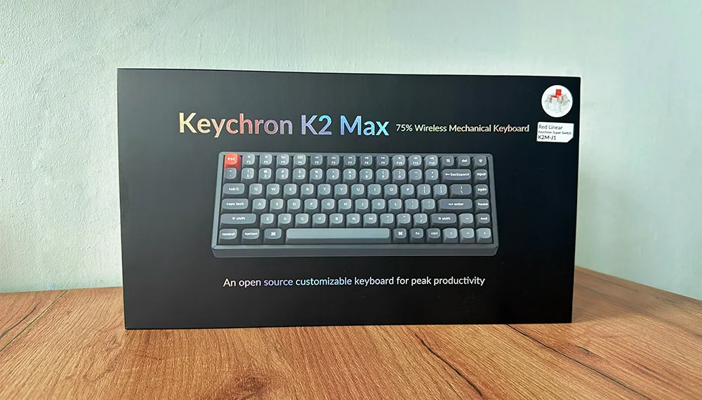 Pudełko Keychron K2 Max QMK na drewnianym blace na tle szarej ściany,