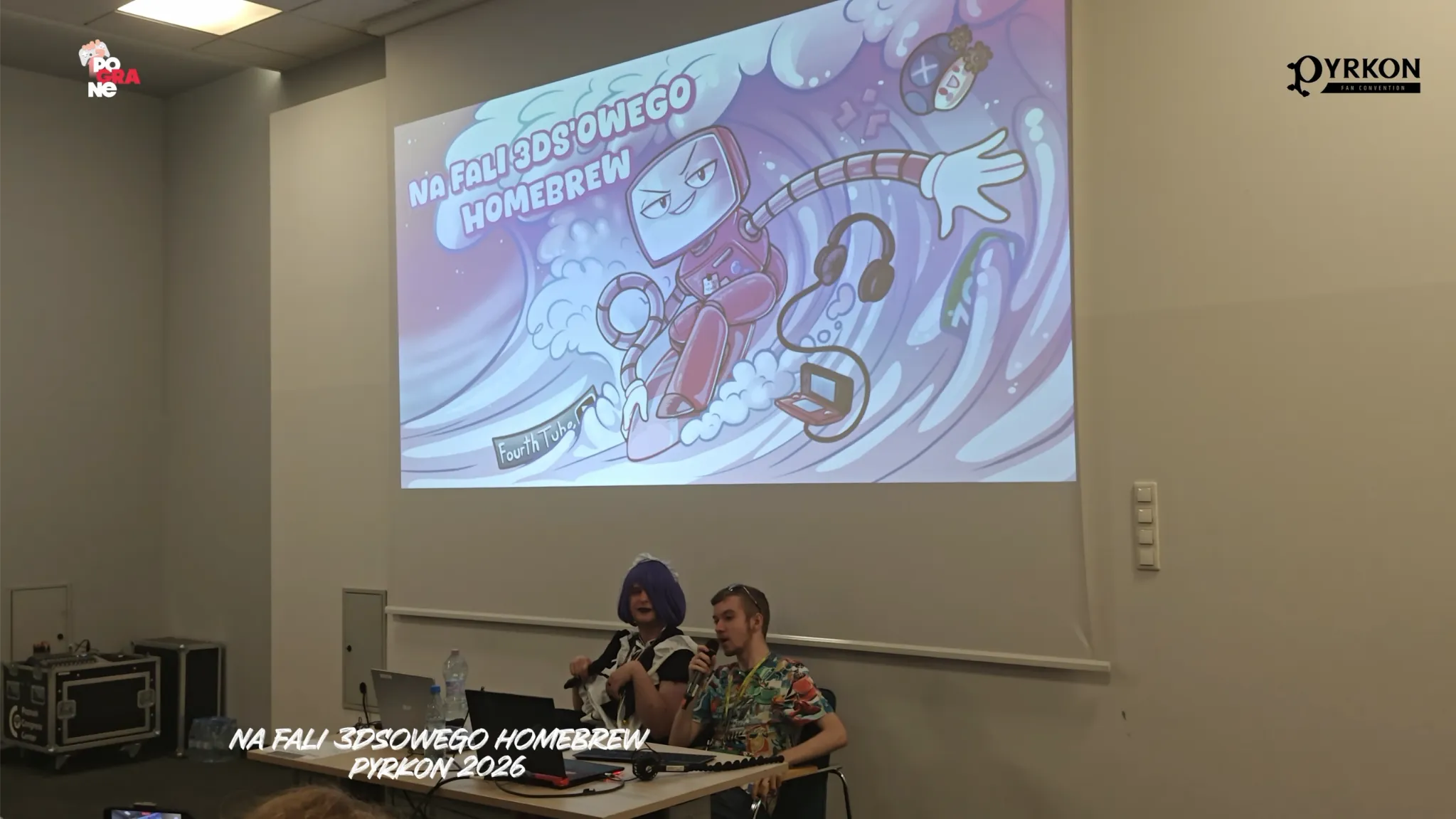 Zdjęcie przedstawia kadr z prelekcji na festiwalu Pyrkon 2026. Na dole kadru nałożono biały podpis: „NA FALI 3DS'OWEGO HOMEBREW PYRKON 2026”. W górnych narożnikach widoczne są logotypy Pograne oraz konwentu Pyrkon.