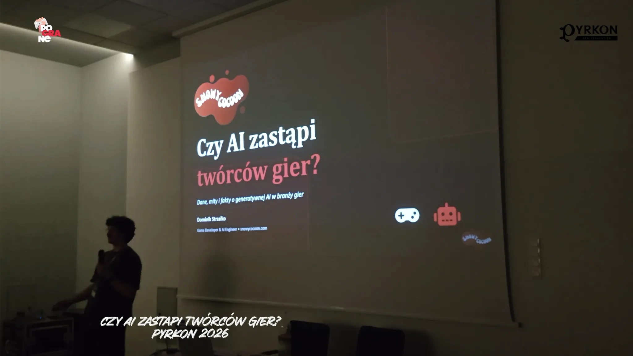 Zrzut ekranu dokumentuje prelekcję poświęconę sztucznej inteligencji w grach. Dolny biały napis głosi: „CZY AI ZASTĄPI TWÓRCÓW GIER? PYRKON 2026”.