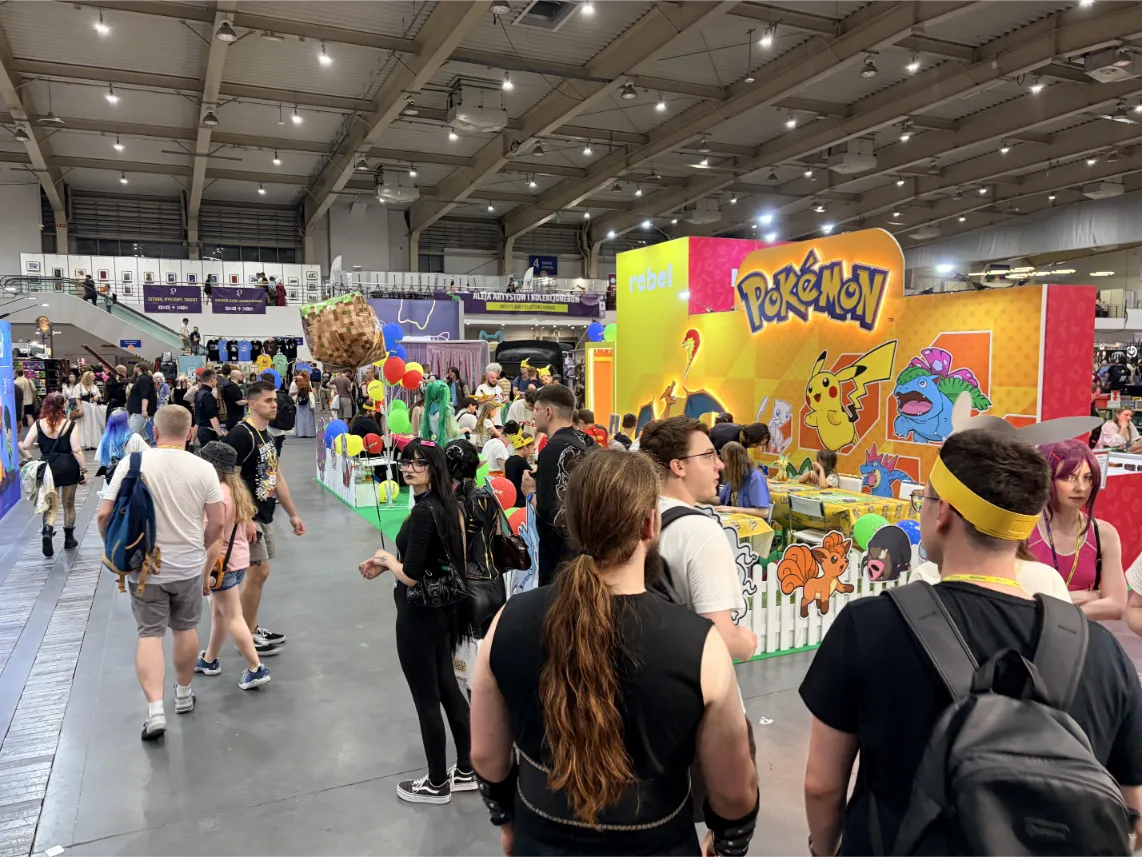 Pyrkon 2026: Kadr prezentuje dużą, jaskrawożółtą strefę tematyczną poświęconą Pokémonom, zorganizowaną przez firmę Rebel, z widocznym z daleka dużym logo oraz grafikami Pikachu i Venusaura.
