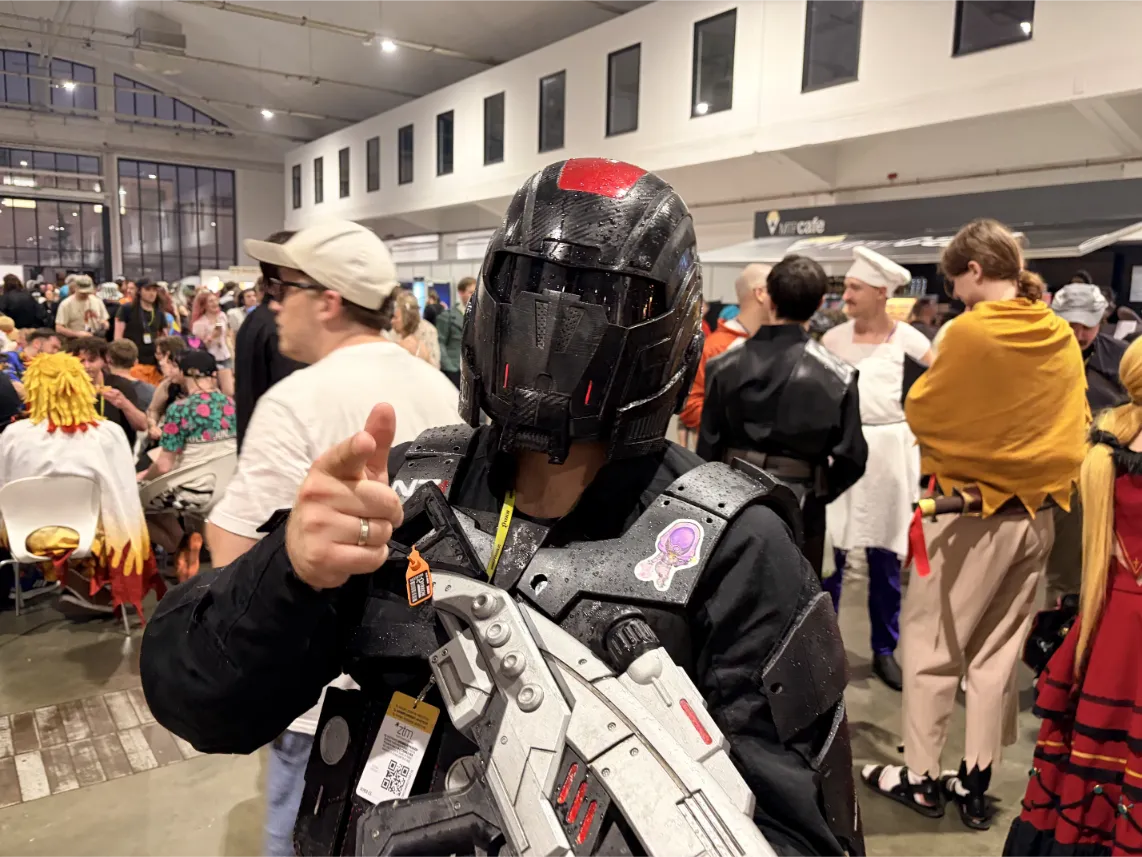 Pyrkon 2026: Ujęcie skupia się na uczestniku w pełnym, czarnym pancerzu science-fiction (stylizowanym na pancerz z Helldivers) z charakterystycznym hełmem z czerwonym akcentem, który celuje palcem wskazującym prosto w stronę widza.