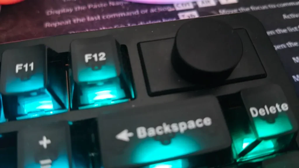 Zbliżenie na metalowe pokrętło funkcyjne oraz podświetlane klawisze F11, F12, Backspace i Delete.