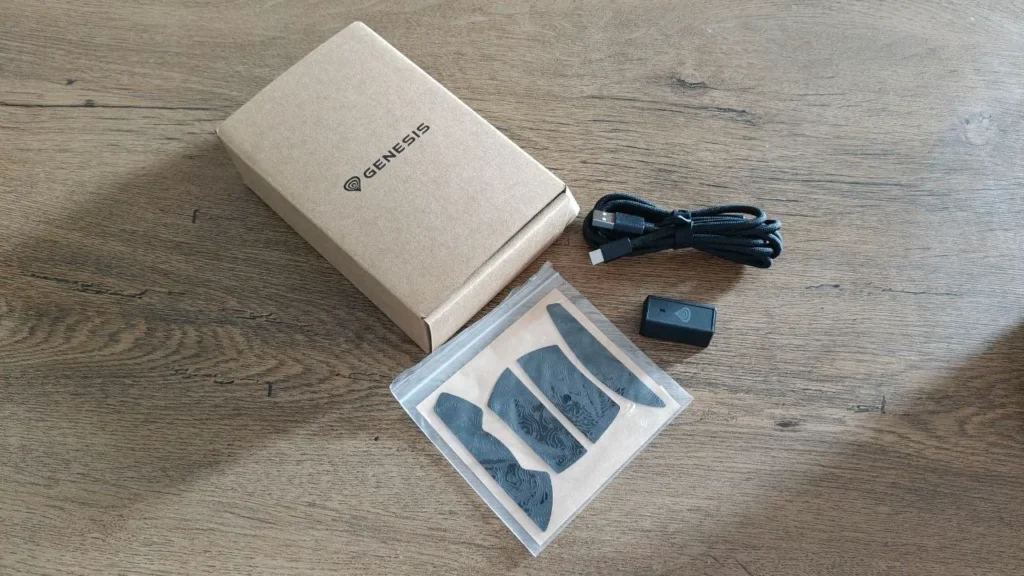 Mysz Genesis Zircon 880 Pro, pudełko, przewód USB, adapter bezprzewodowy i dodatkowe ślizgacze na drewnianym biurku.