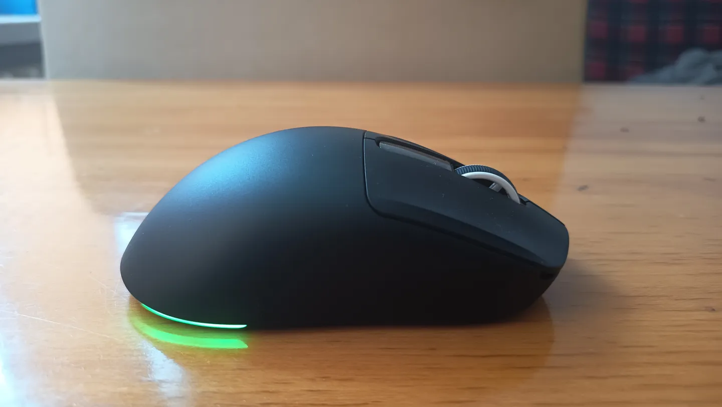 Zbliżenie na czarną mysz gamingową Epomaker NEX Lite z podświetleniem RGB, widoczną z profilu na drewnianym biurku.