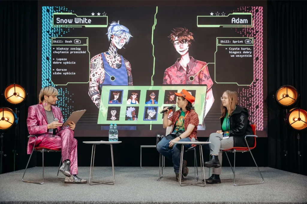 Panel dyskusyjny na scenie konwentu z udziałem trzech osób na tle telebimu prezentującego ekran wyboru postaci z gry z profilami Snow White i Adama.