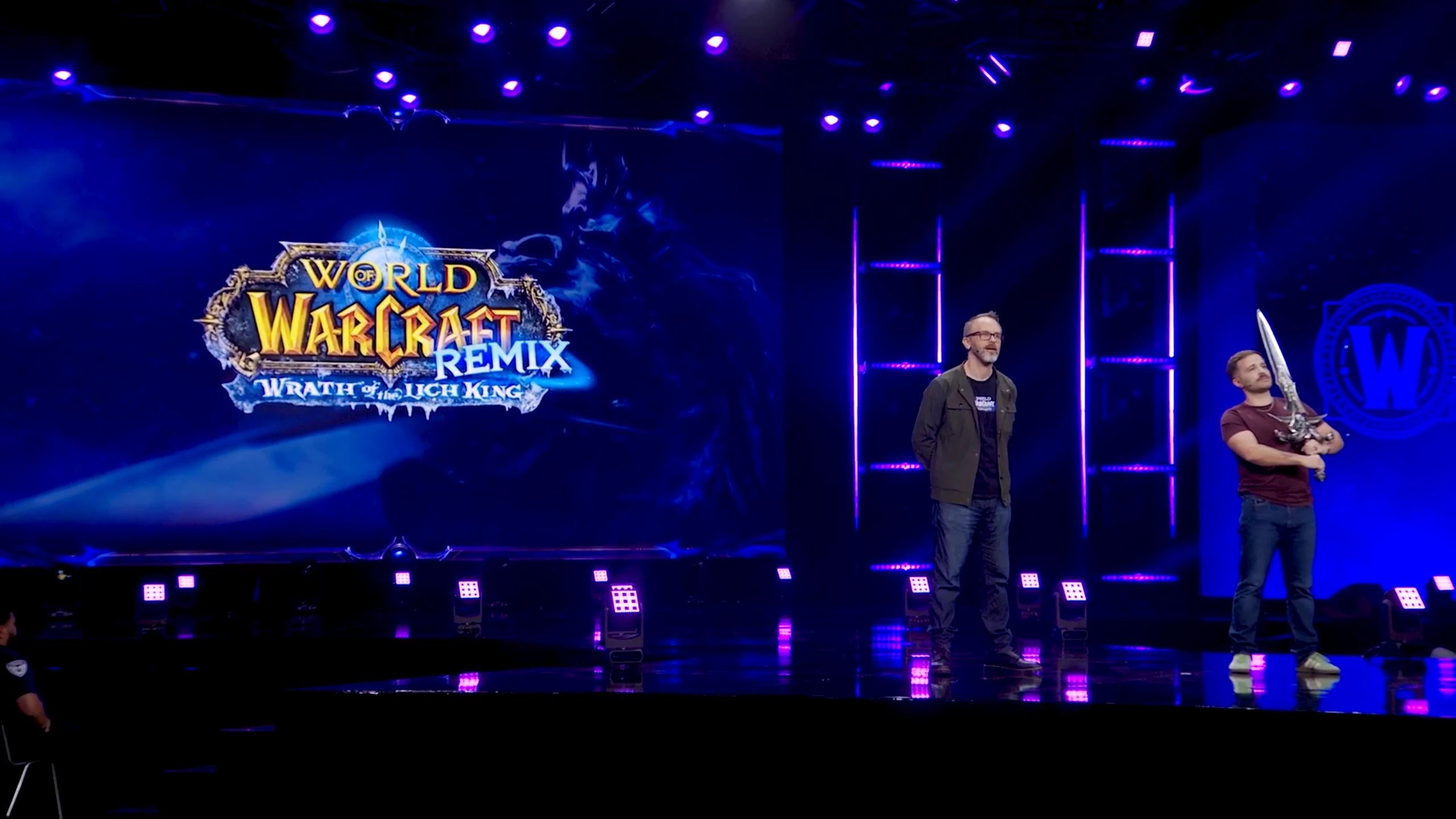 Kadr z prezentacji World of Warcraft zapowiadający „Wrath of the Lich King Remix”; na scenie stoją dwaj prezenterzy, a na ekranie widnieje logo wydarzenia.