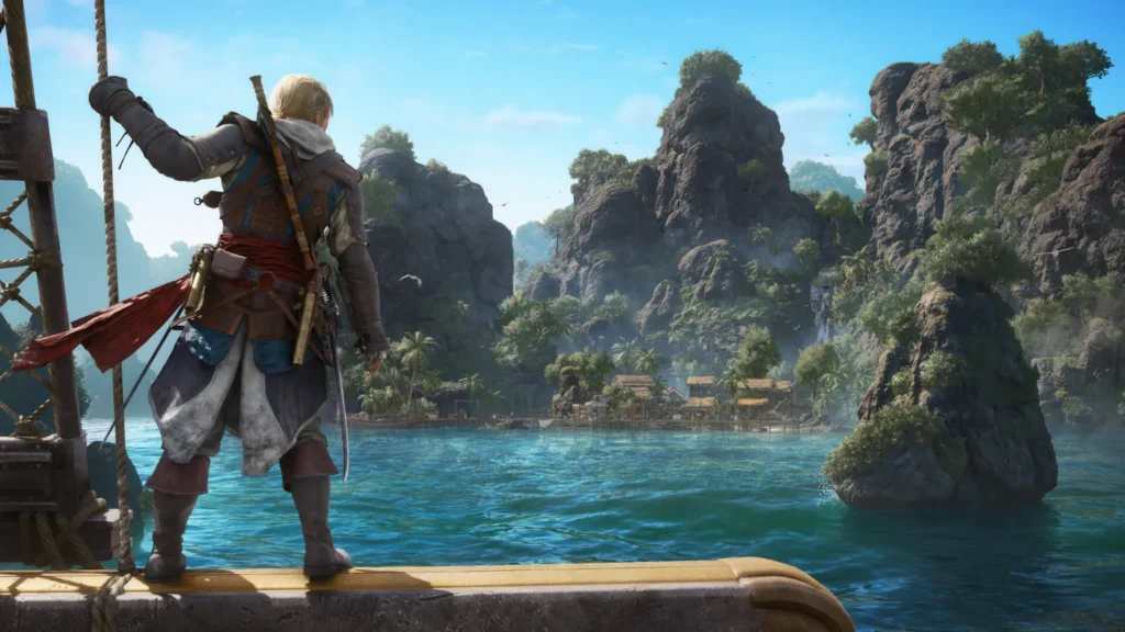 Edward Kenway stojący na dziobie statku i spoglądający na tropikalną zatokę z osadą u stóp skalistych wzgórz.