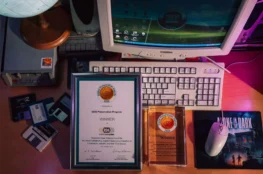 Dyplom i statuetka Digital Preservation Awards 2026 dla GOG Preservation Program leżące na biurku obok retro komputera PC, dyskietek i stacji dysków.