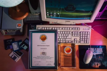 Dyplom i statuetka Digital Preservation Awards 2026 dla GOG Preservation Program leżące na biurku obok retro komputera PC, dyskietek i stacji dysków.
