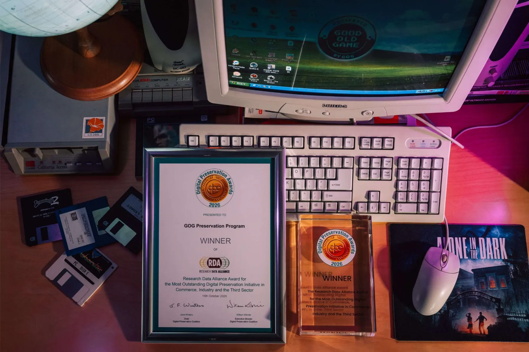 Dyplom i statuetka Digital Preservation Awards 2026 dla GOG Preservation Program leżące na biurku obok retro komputera PC, dyskietek i stacji dysków.