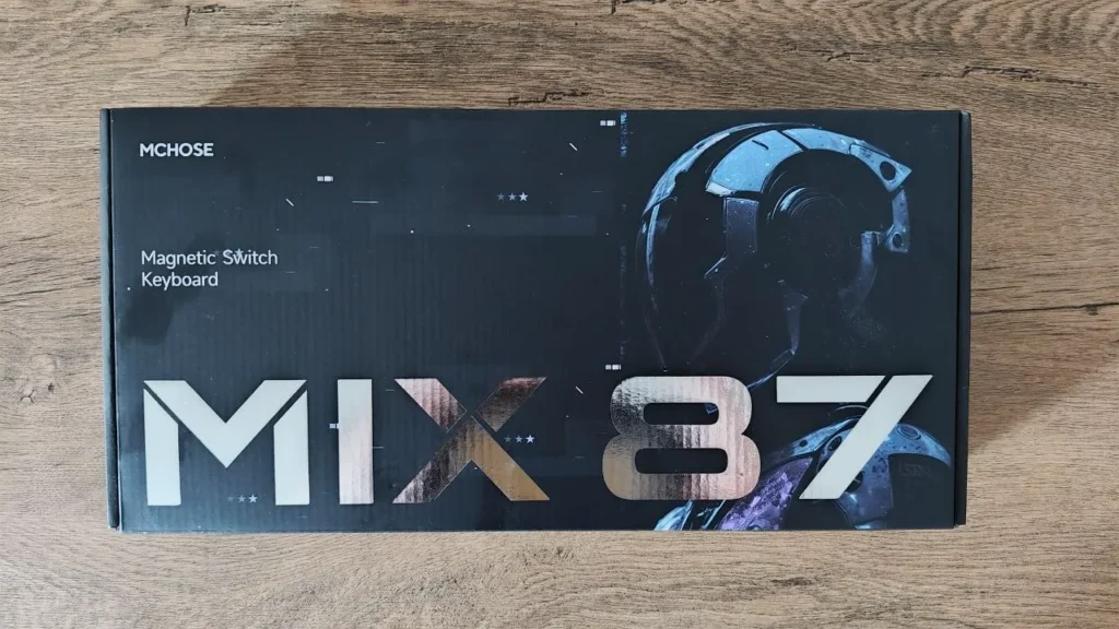 Czarne pudełko klawiatury magnetycznej MCHOSE MIX 87 z dużym, srebrzystym napisem modelu leżące na drewnianym stole.