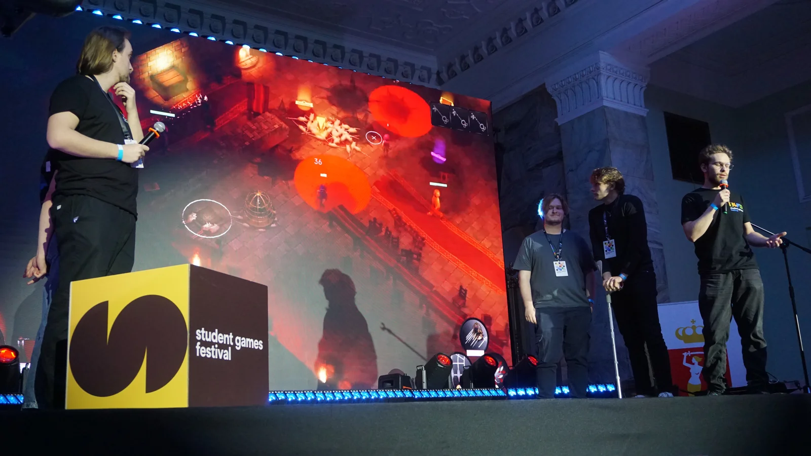 Pięć osób na scenie podczas festiwalu studentów gier, za nimi ekran z prezentacją.